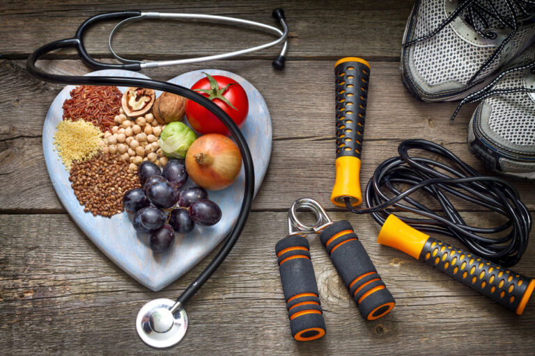 Lifestyle Medicine with heart shaped board with healthy foods, sneakers, weights, and a stethescope